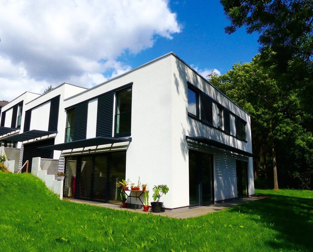 Bâtiment moderne blanc à plusieurs étages avec des volets noirs et des fenêtres panoramiques dans un jardin verdoyant