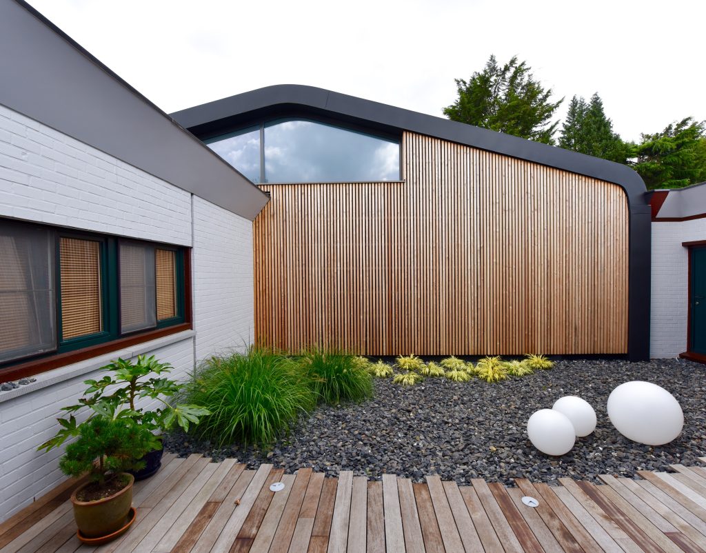 Bâtiment architectural moderne avec revêtement en bois, jardin avec sphères lumineuses et terrasse en bois