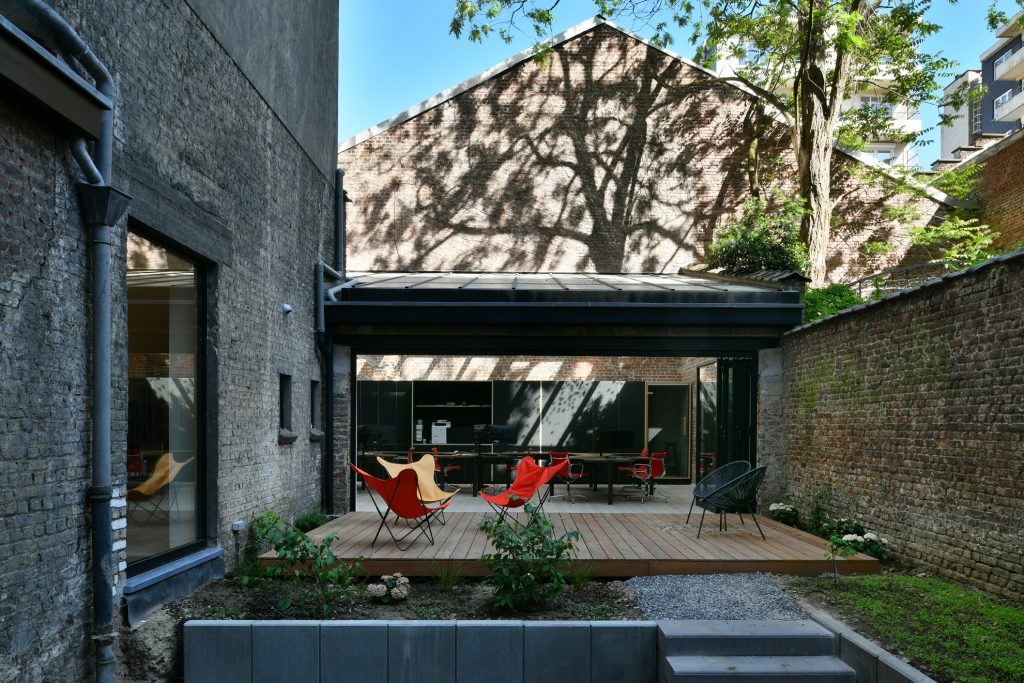 Terrasse en bois avec chaises papillon oranges et jaunes devant un espace intérieur avec bureaux