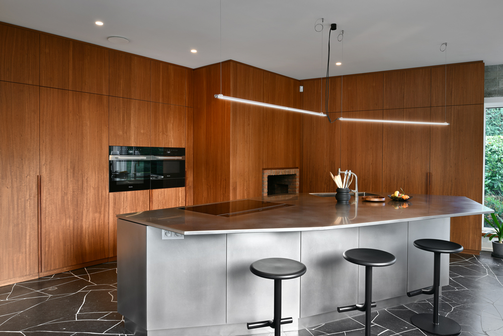 Cuisine moderne avec îlot central en métal, plan de travail en inox, et placards muraux en bois chaleureux avec deux fours intégrés