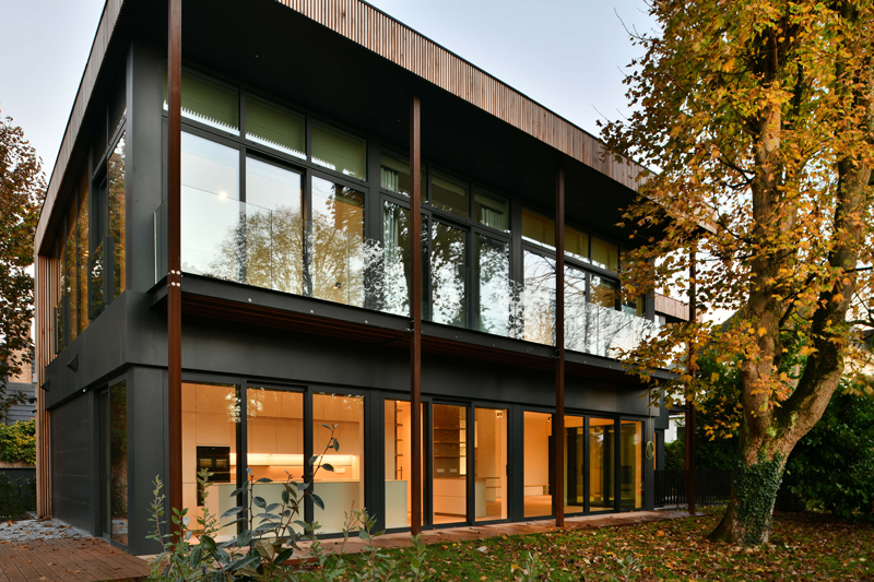 Maison contemporaine vitrée à deux étages entourée d’arbres en automne