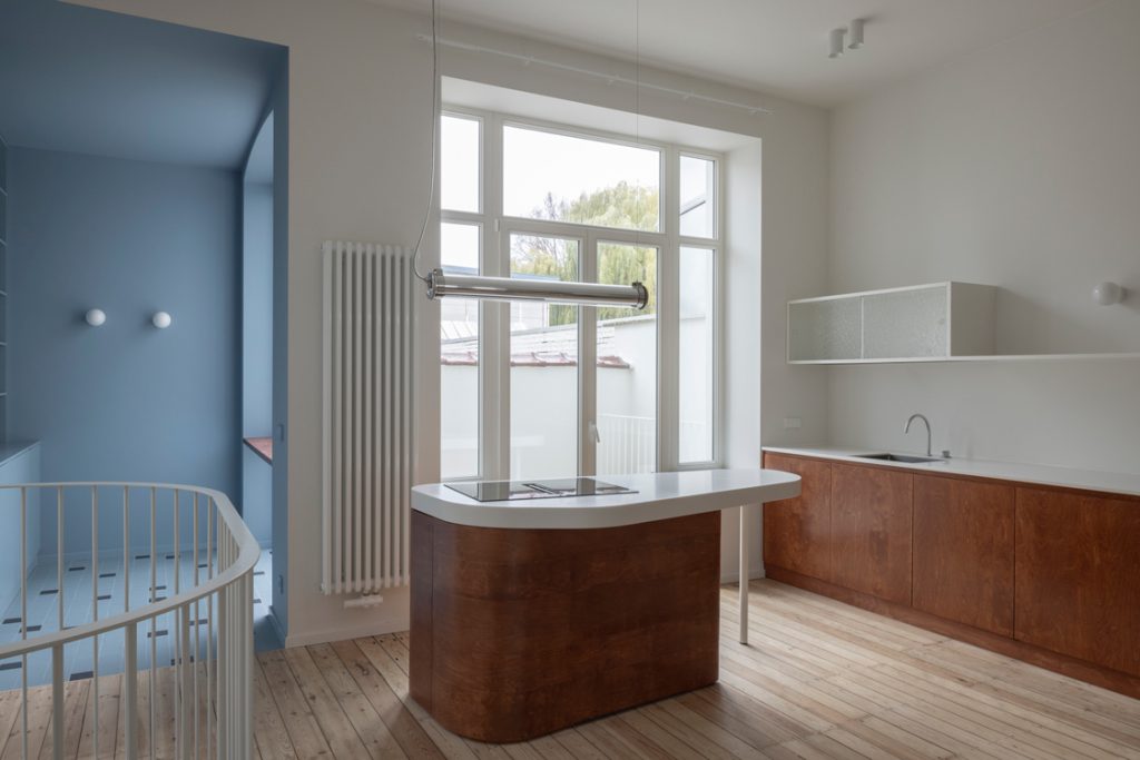 Cuisine lumineuse avec îlot central, meubles en bois, grande fenêtre et escalier bleu