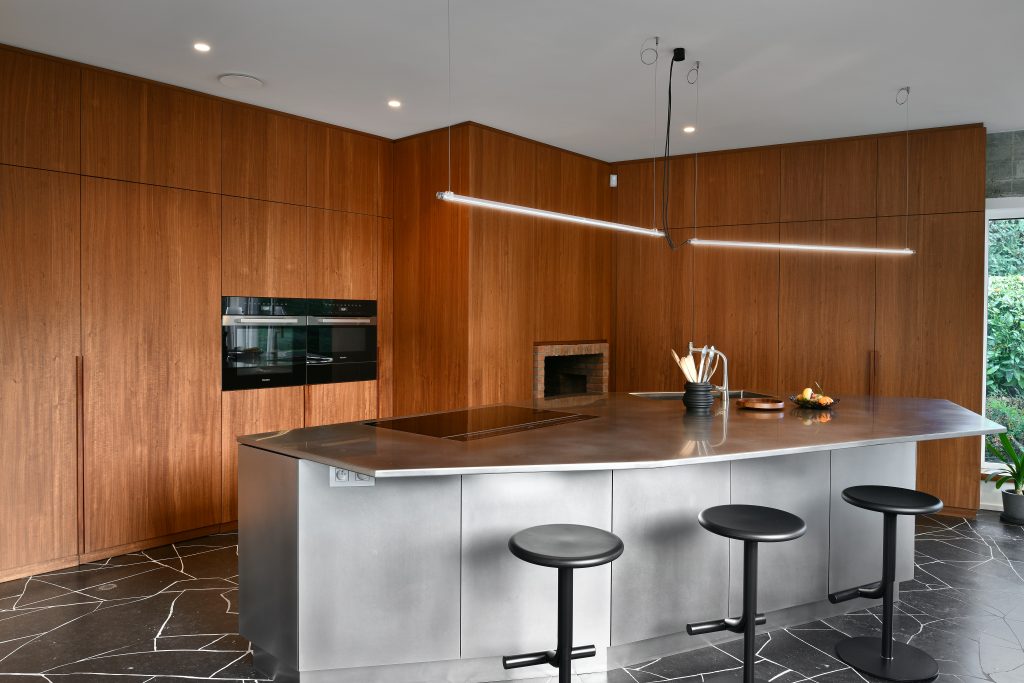 Cuisine moderne avec îlot central en métal, plan de travail arrondi, et revêtements muraux en bois.